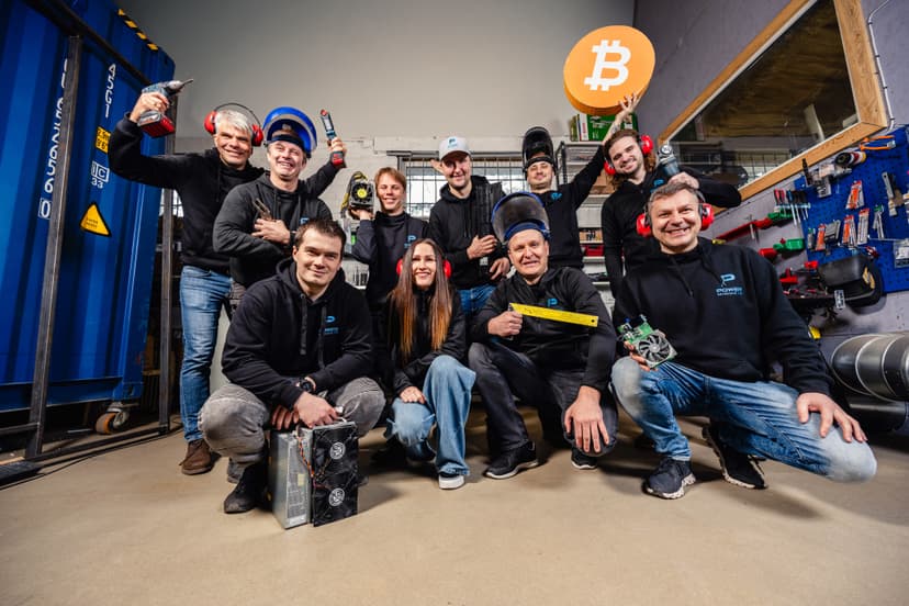 Komandas bildes (10 cilvēki). Fonā redzams konteiners. Viens cilvēks tur rokā Bitcoin zīmi