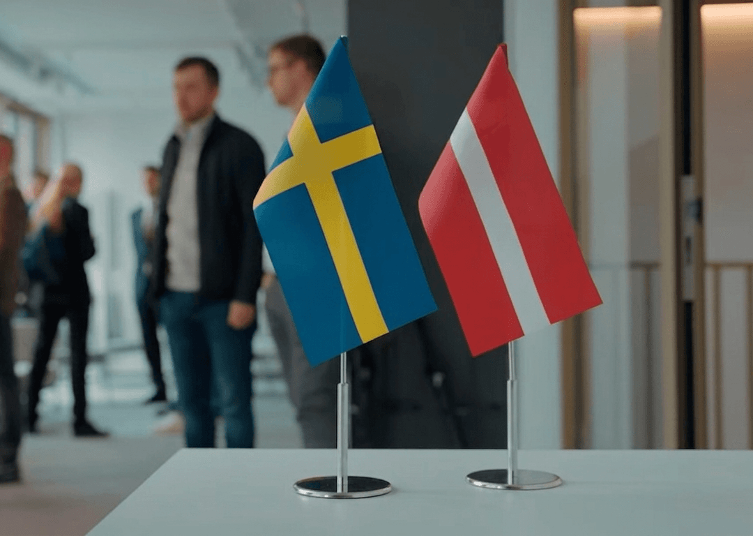 LIAA organizē Latvijas uzņēmēju tirdzniecības misiju uz Zviedriju Latvijas un Zviedrijas karodziņi, kas stāv uz galda. Fonā redzami uzņēmēji sarunājamies viens ar otru